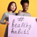 Two women holding a sign with '#healthy habits' on a vibrant yellow background.